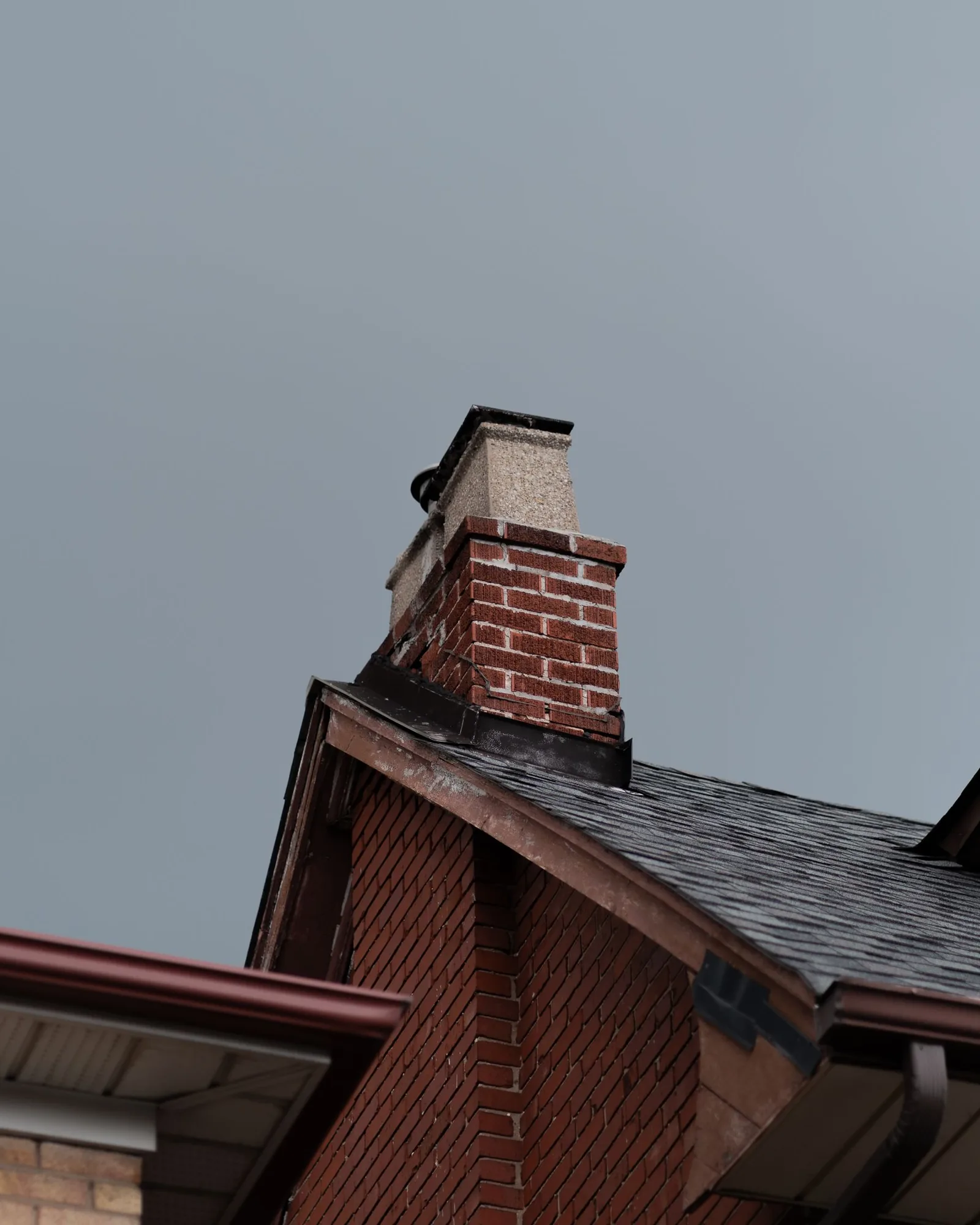 Brick chimney rising above a gabled shingle roof against a gray sky
