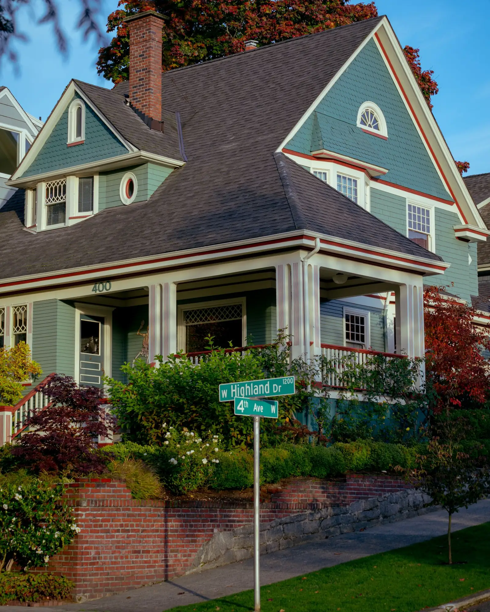 Blue-gray Craftsman house with a brick chimney and deep porch on a Seattle corner