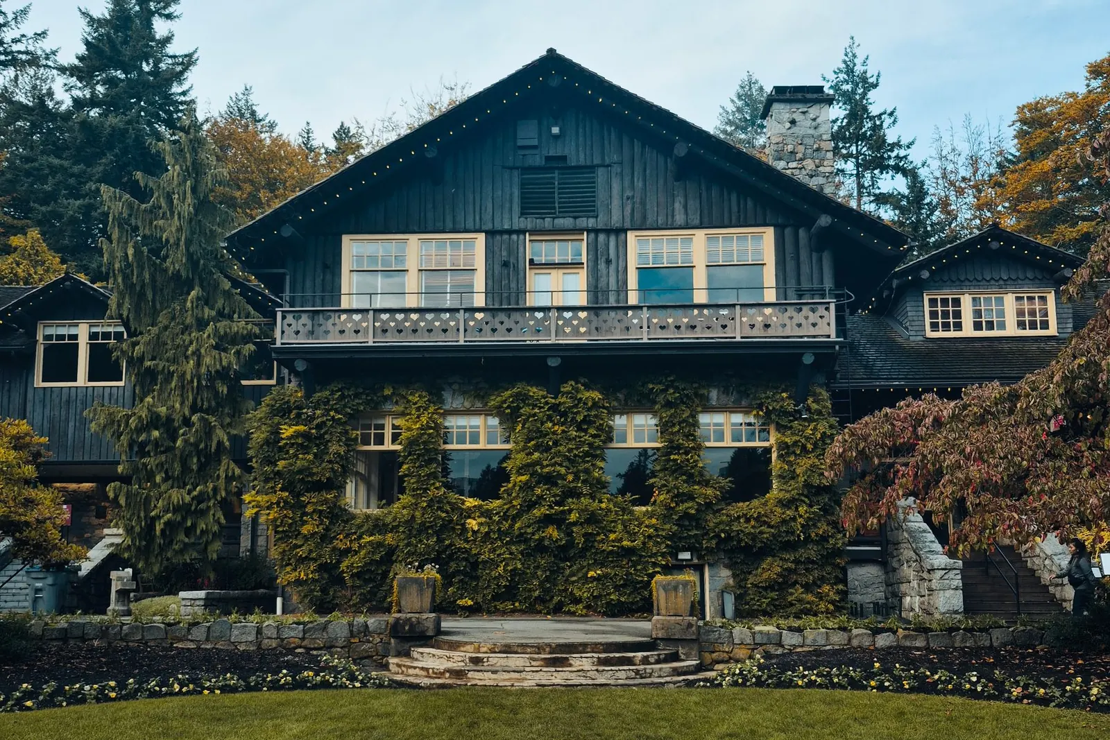 Dark-shingled heritage house with a chimney among tall evergreens and lawn