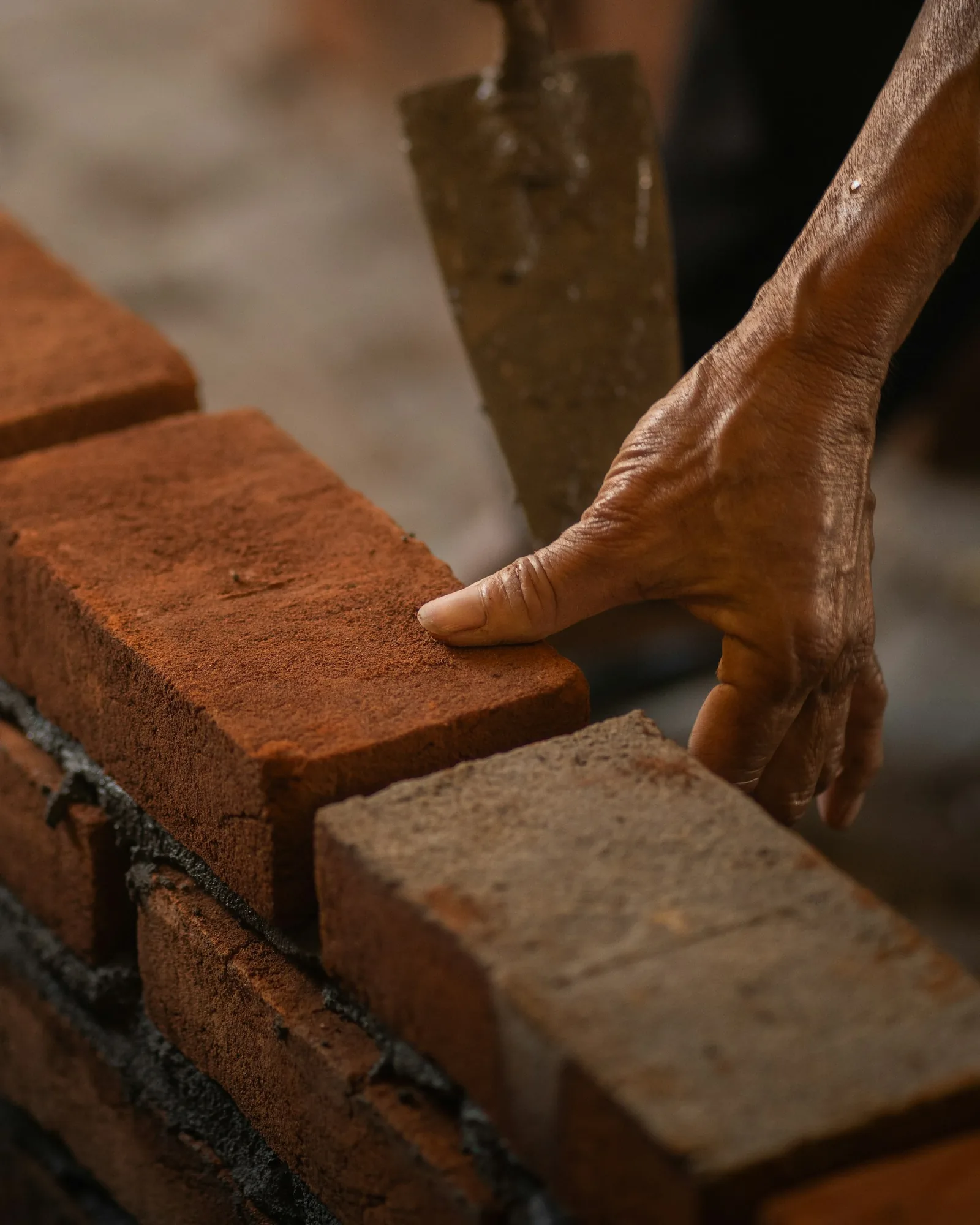 Mason hand setting a red brick beside a trowel on fresh mortar