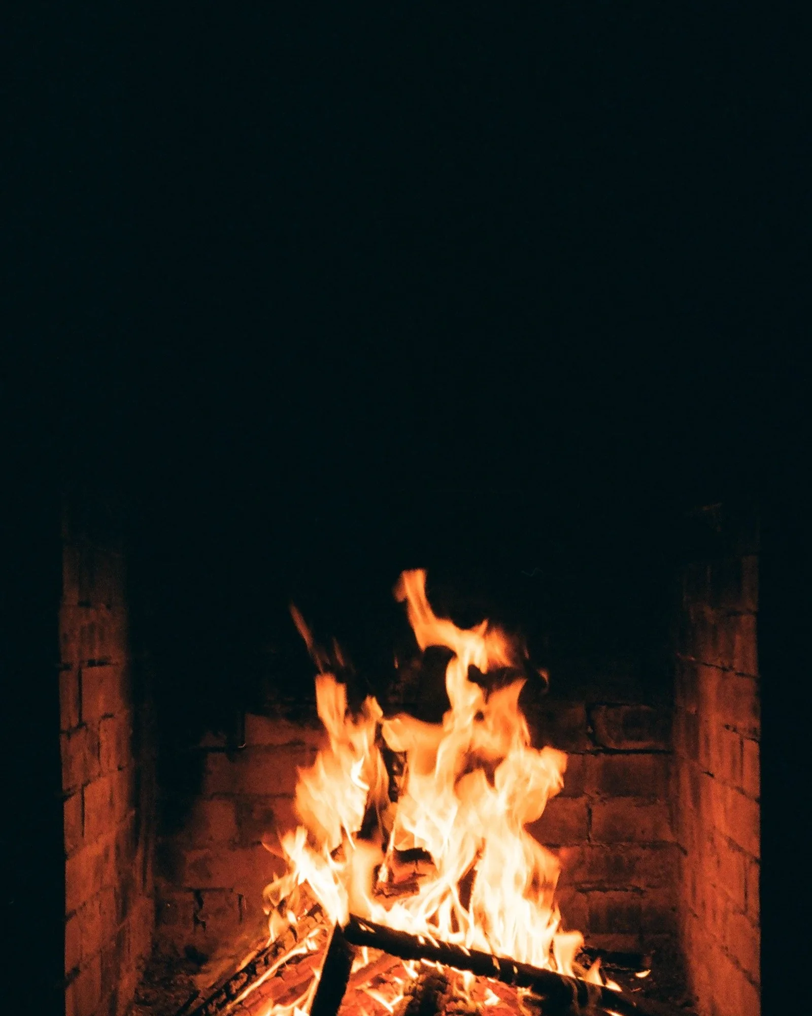 Wood logs burning brightly inside a dark brick firebox